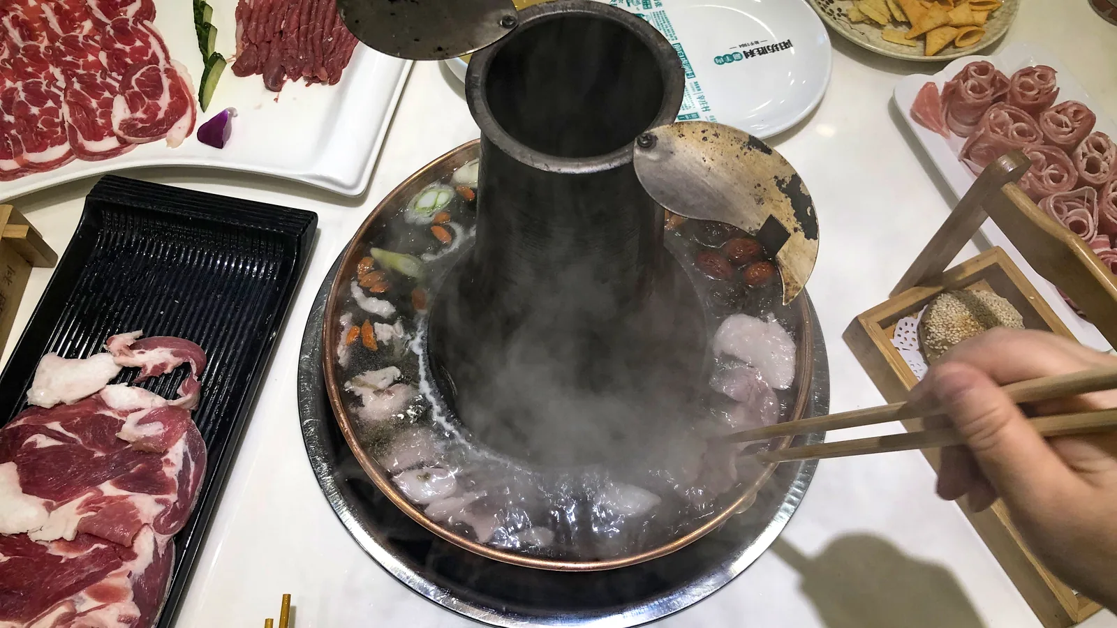 Traditional chimney-shaped copper hotpot surrounded by sliced lamb