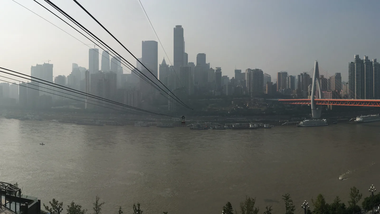 Cableway lines and a cabin crossing the Yangtze with Chongqing skyline beyond